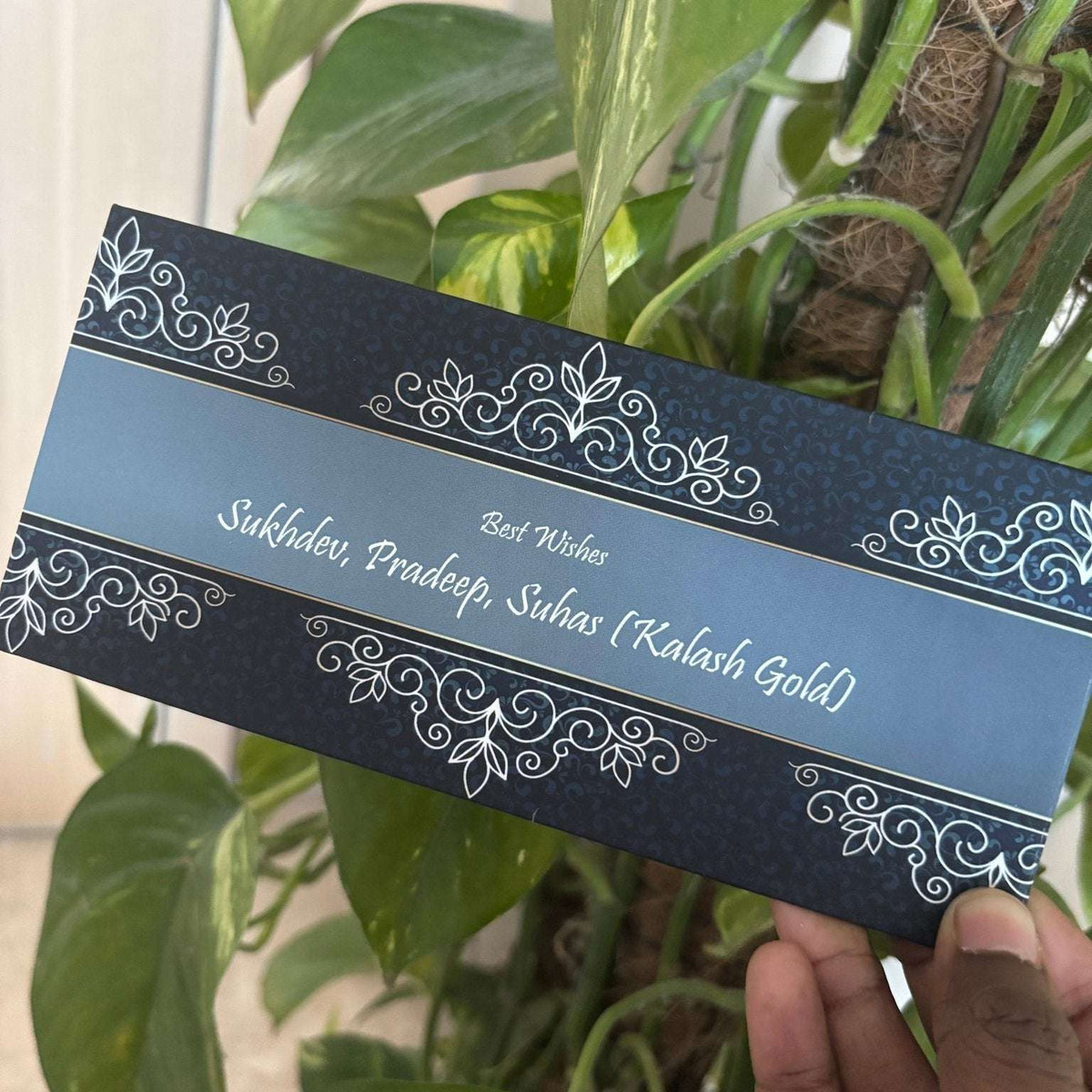 Decorative envelope with intricate designs held by a hand against a green leafy background