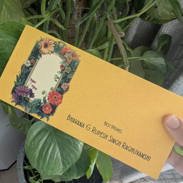 Yellow envelope with floral design held by a hand in front of green plants