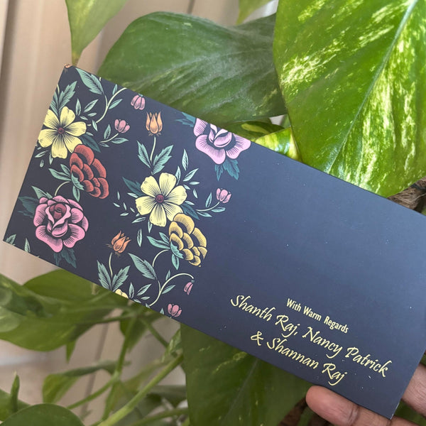 Floral design on a blue black envelope held by a hand with green leaves in the background