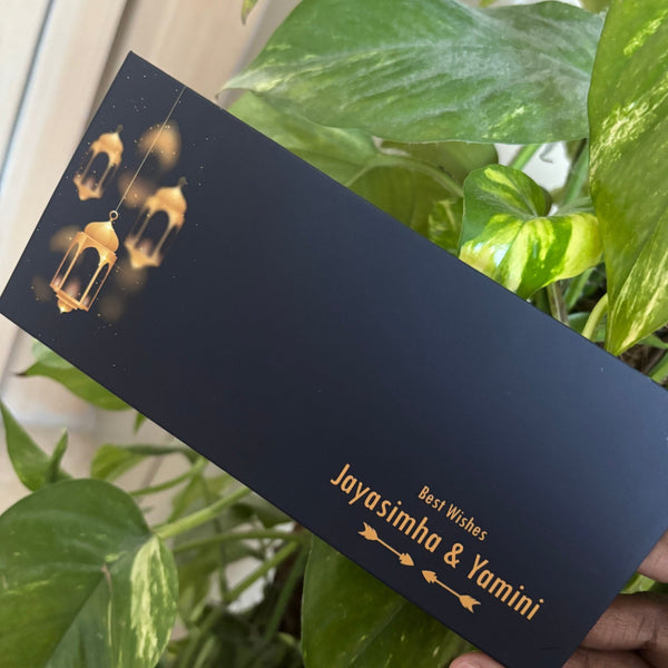 Hand holding a lanterns theme envelope with gold text against a green leafy background