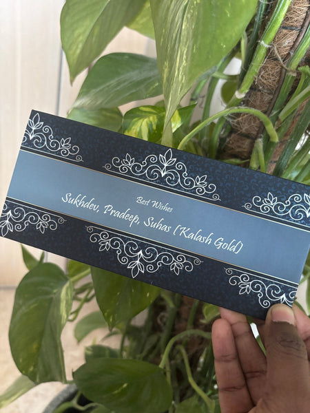 Decorative envelope with intricate designs held by a hand against a green leafy background
