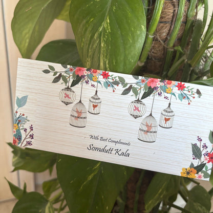 Card with floral and bird design held by a hand against a green leafy background
