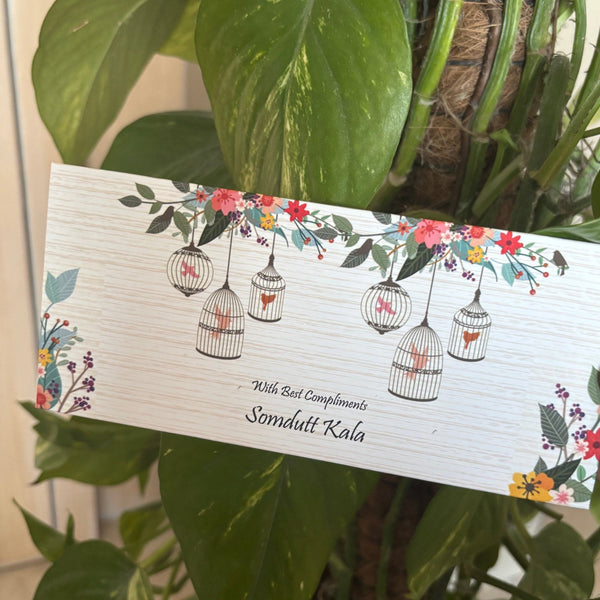 Card with floral and bird design held by a hand against a green leafy background