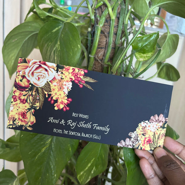 Floral-themed business card held by a hand in front of a green plant