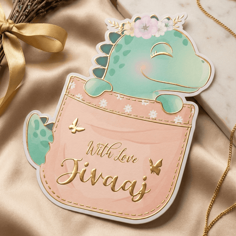 GIft tag/sticker with a dinosaur design and gold embossed 'With love Jivaaj' text  on a soft fabric background.