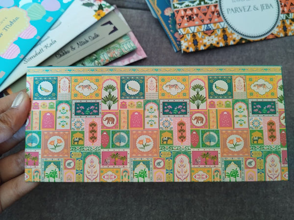 Decorative envelope with a colorful Indian pattern held by a hand on a dark surface